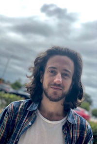 a man with long hair standing in front of a cloudy sky